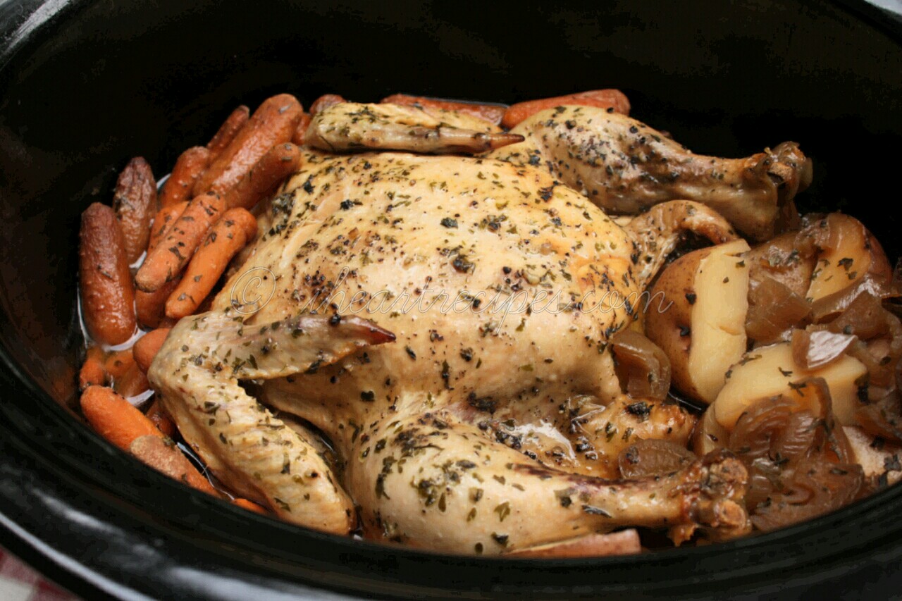 An overhead image of a slow-cooked chicken seasoned with herbs and spices, and tender carrots, onions, and potatoes in a crockpot.