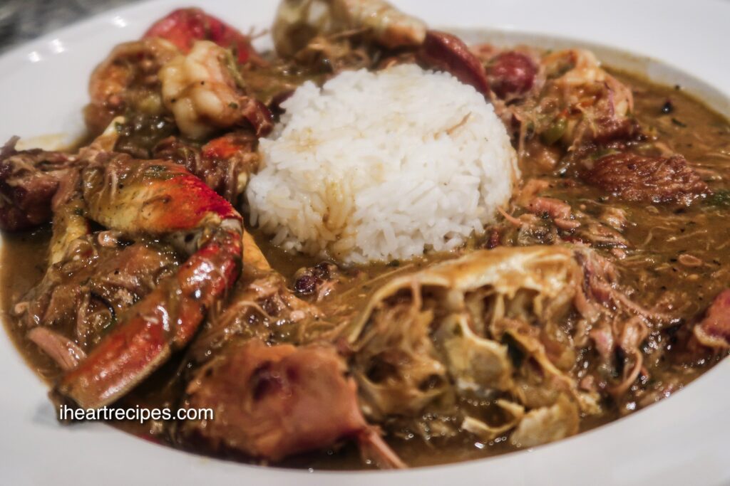 A shallow white bowl filled to the brim with Smoked Turkey Gumbo with a scoop of white rice in the middle.