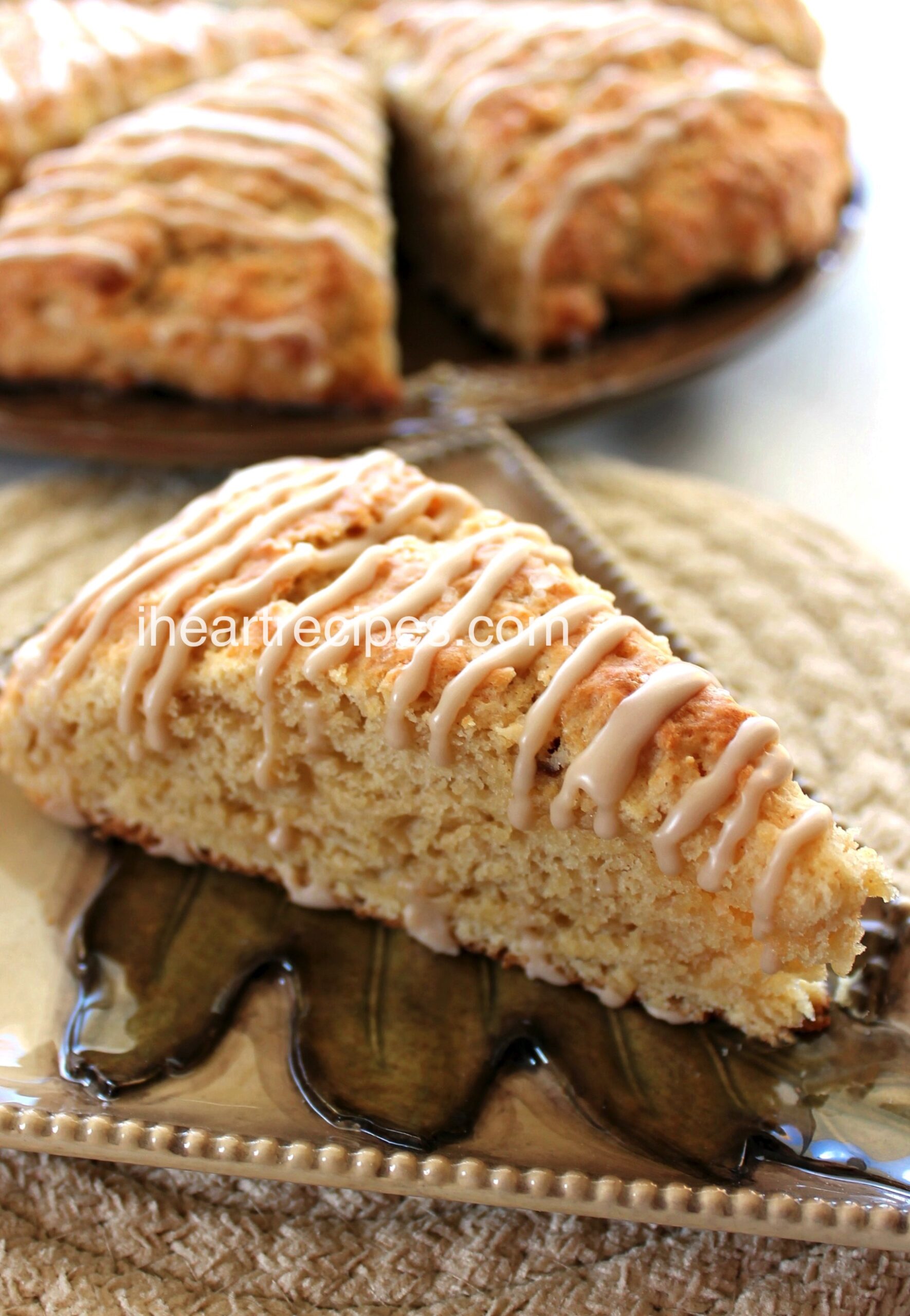 A closeup image of a homemade brown butter maple scone, drizzled with a vanilla maple icing and served on a ceramic plate.