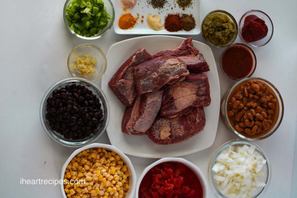 All of the ingredients for slow cooker beef brisket chili separately arranged on a white countertop. 
