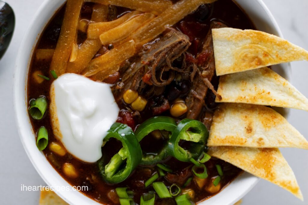 Slow Cooker Beef Brisket Chili garnished with fresh sliced jalapeños, pita chips and a dollop of sour cream. 