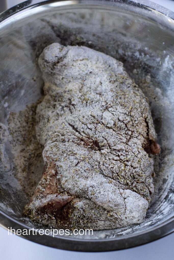 A roast dredged in flour and seasoning resting in a silver bowl. 