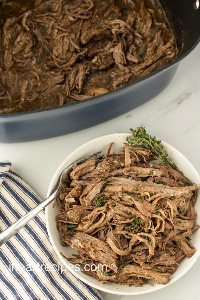 A white bowl filled with slow cooker tri-tip roast. A fork rests alongside the roast.