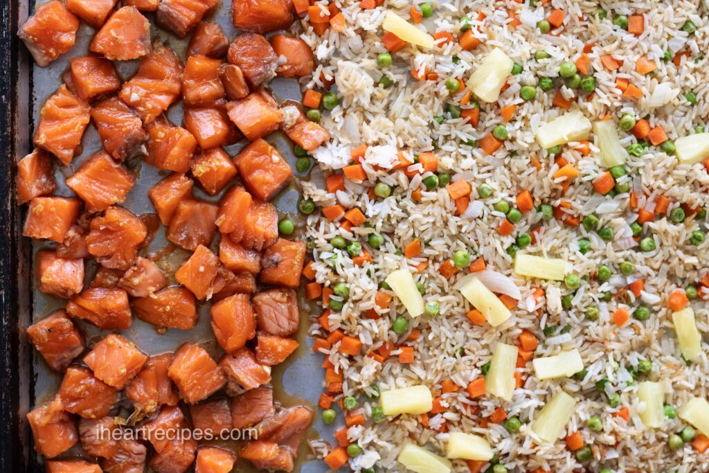 Rice and veggies cover half of a sheet pan and pink salmon chunks coated in teriyaki sauce cover the other half. 