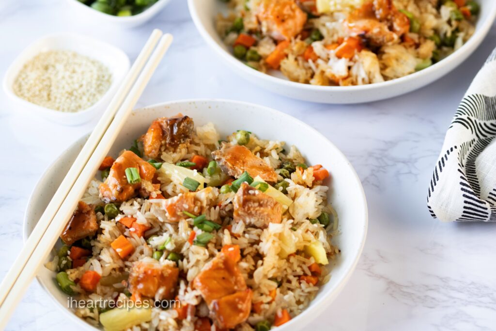 Two bowlfuls of Teriyaki Salmon Sheet Pan Fried Rice. Wooden chopsticks rest on one of the bowls.