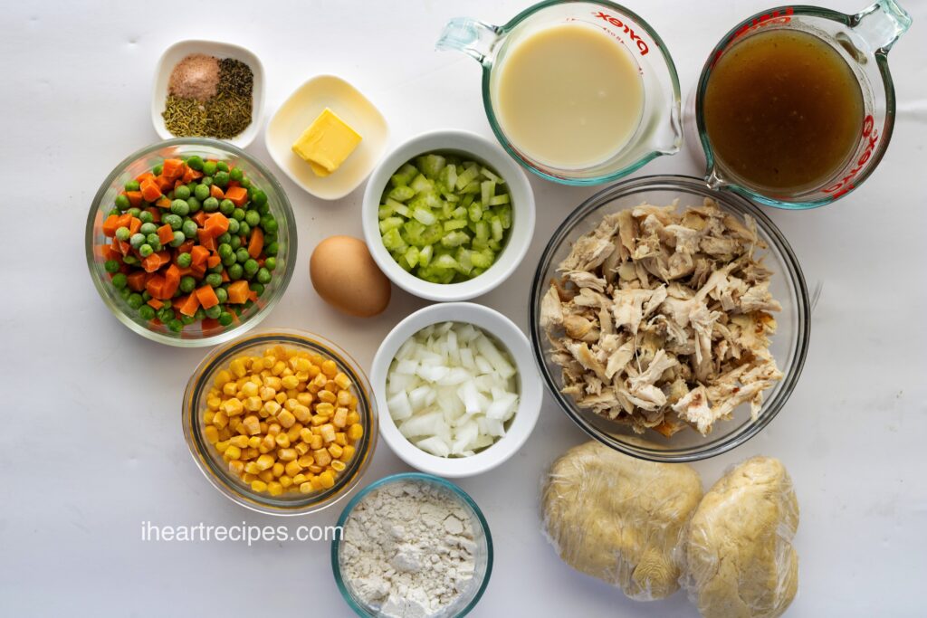 Ingredients for pot pie separated in small bowls set on a white marble countertop. 