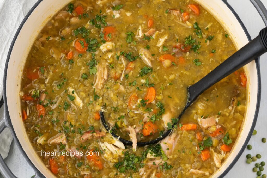 An overhead image of a large cast iron pot filled with Smoked Turkey Split Pea Soup. A black ladle is submerged in the soup.