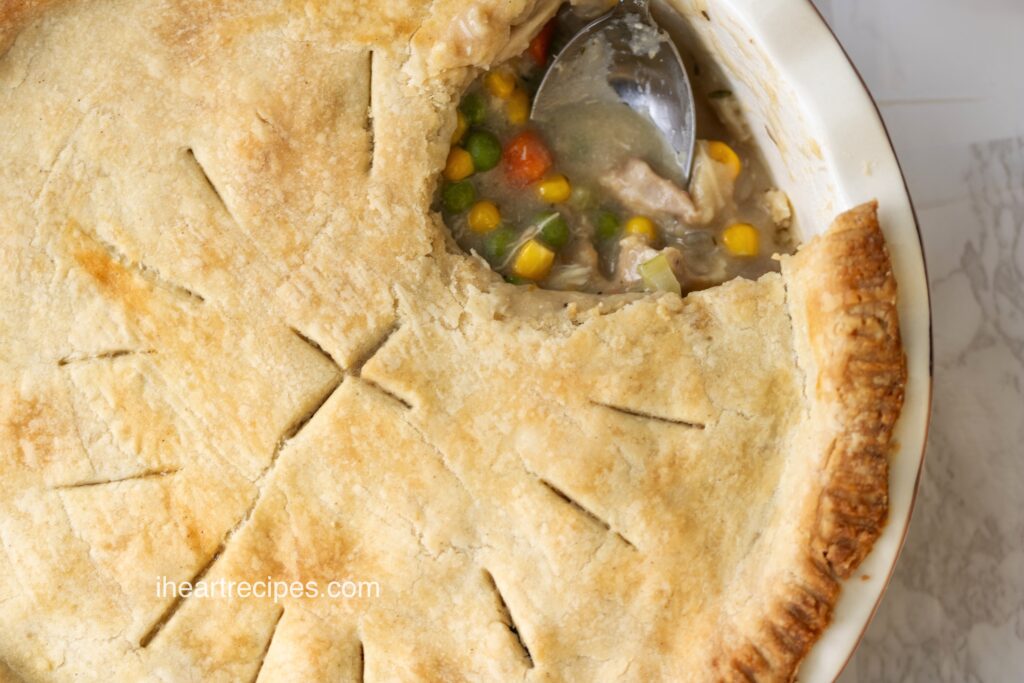 A large leftover turkey pot pie with a scoop removed by a silver spoon. 