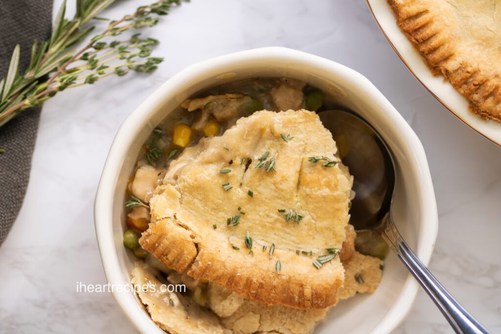 A serving of golden and savory leftover turkey pot pie in a white bowl. A silver spoon rests next to the pot pie.