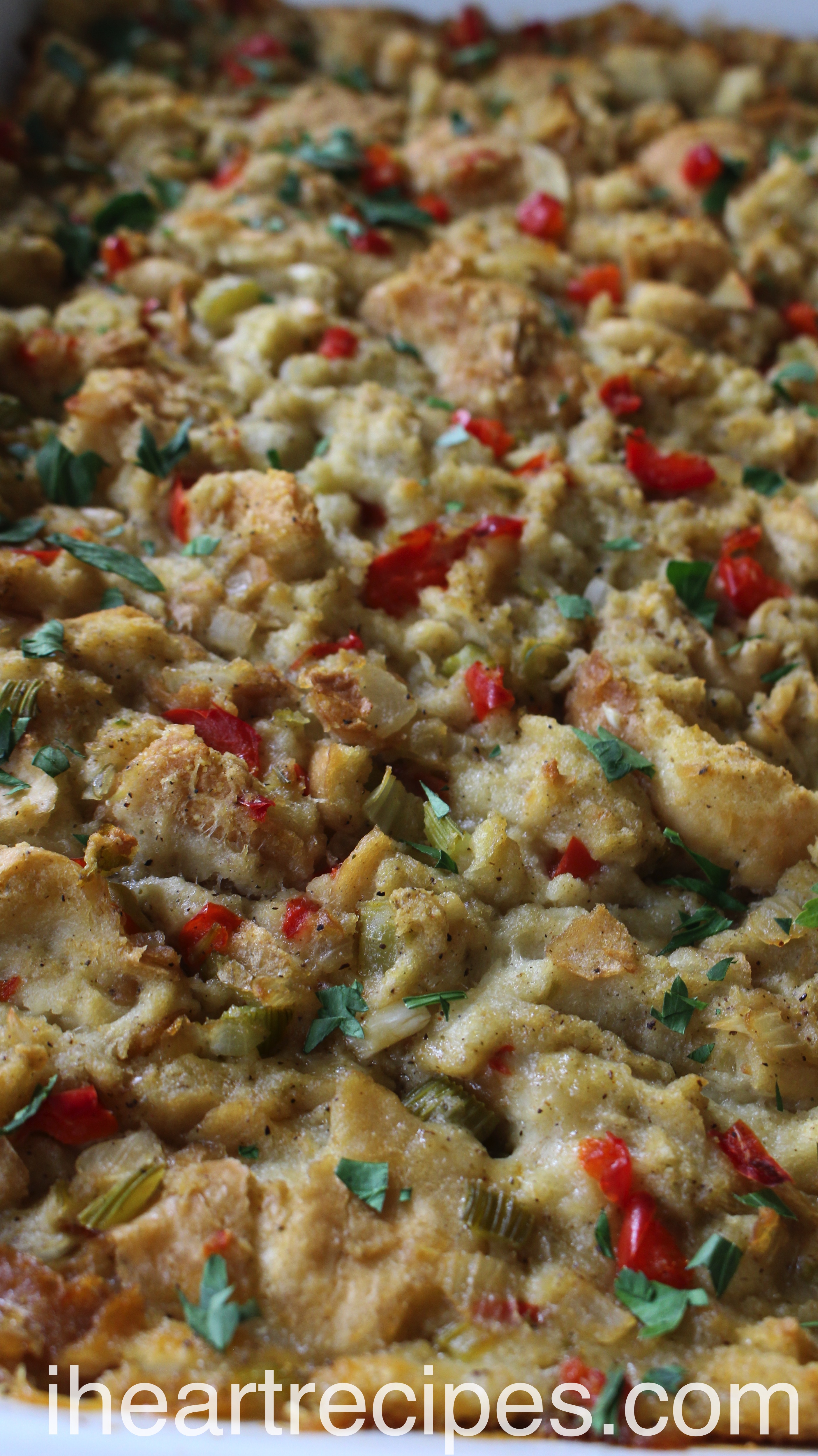 A closeup image shows a casserole dish filled with homemade stuffing. This stuffing recipe is made with French bread, onions, celery, and red bell peppers and baked to golden-brown perfection.