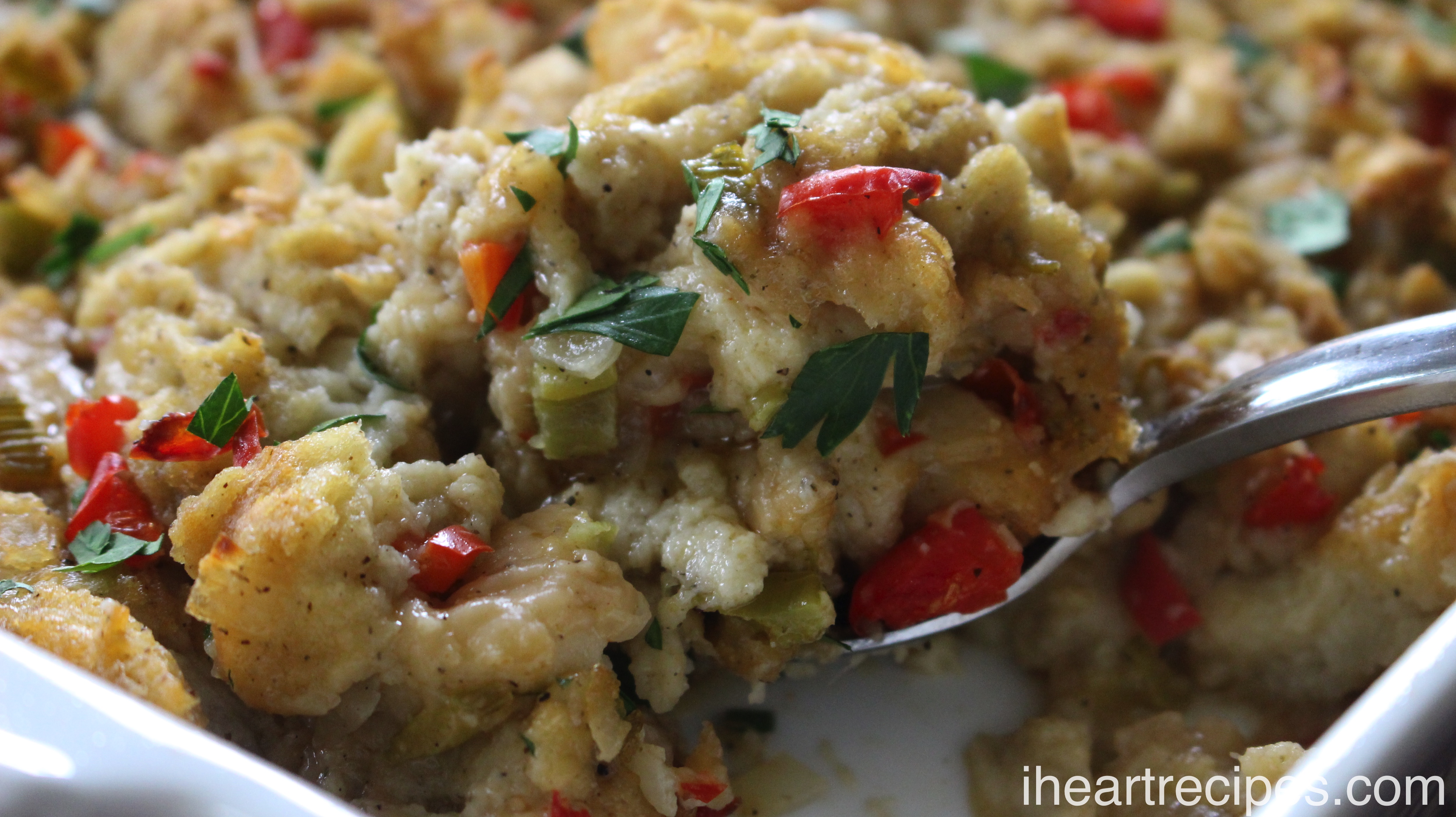 A silver serving spoon scoops up a spoonful of homemade stuffing baked in a white casserole dish.