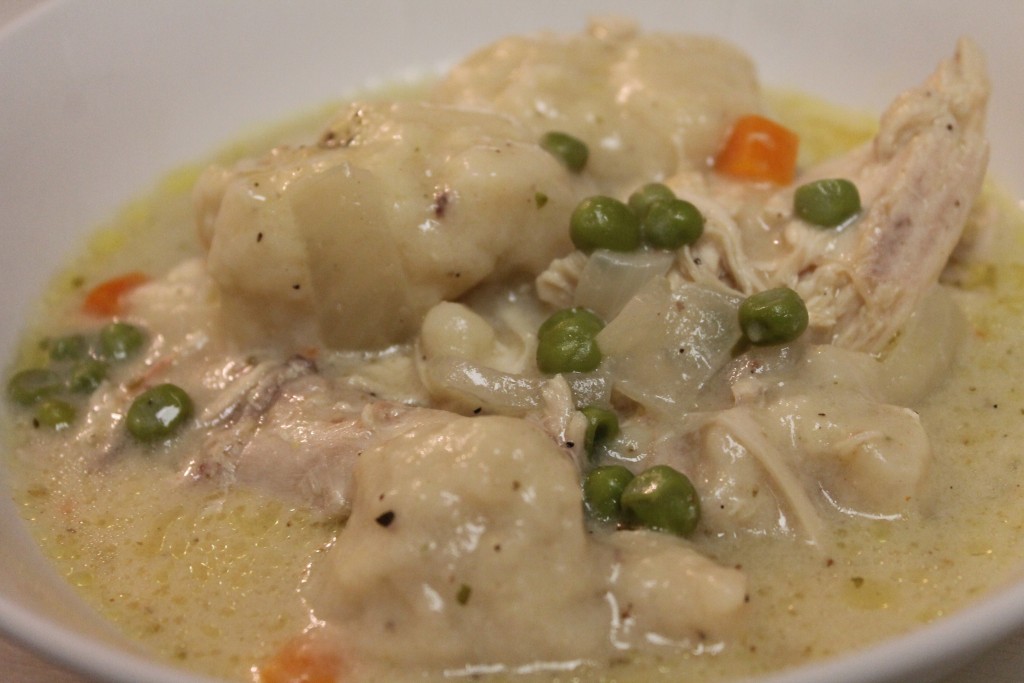 A large bowl of homemade chicken and dumplings slow cooked in a creamy broth with onions, carrots, and peas.