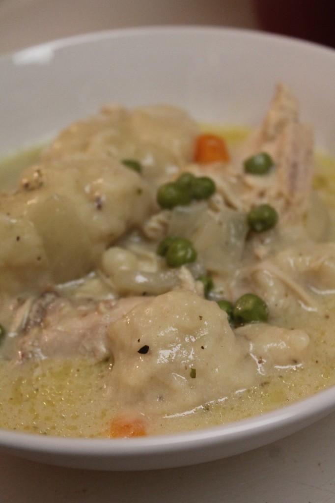 Golden dumplings, tender chicken and colorful veggies in a comforting broth fill a large white bowl. 