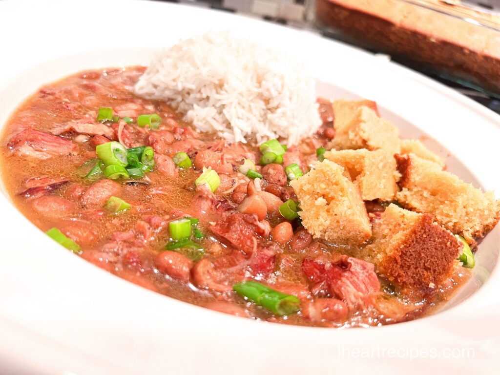 A shallow white bowl filled with southern pinto beans, a mound of rice and cubed corn bread.