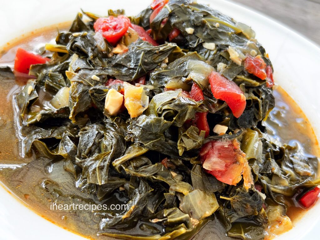 Bright greens and tender tomatoes in a savory broth served in a white bowl.  