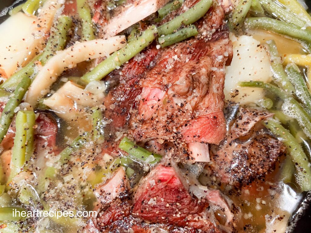 A close-up image of greens beans, potatoes, and smoked neck bones in a well-seasoned broth.