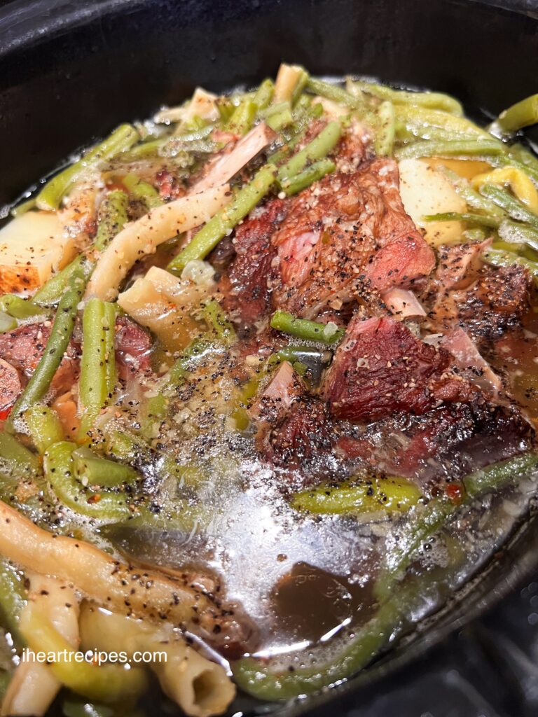 Tender meat, bright veggies and soft potatoes in a black slow cooker. 