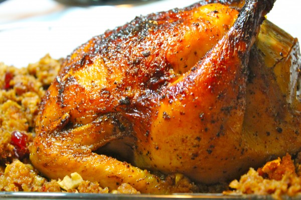 A closeup image of a whole apple glazed chicken served with homemade bread stuffing.