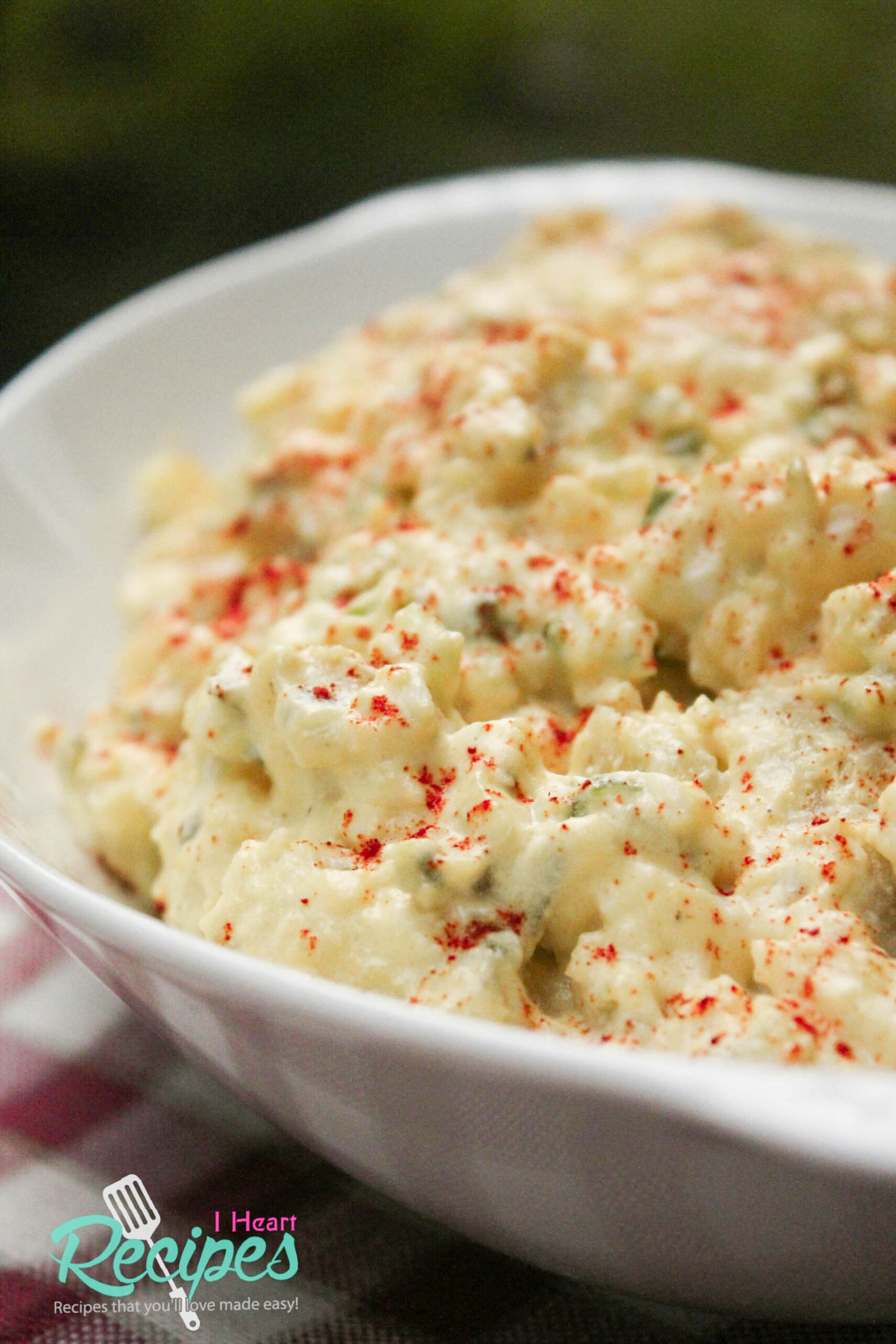 A close up image of a dish of classic creamy potato salad, garnished with a sprinkle of paprika.