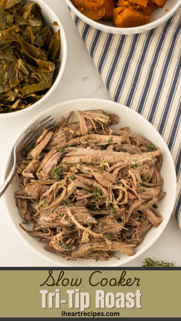 Shredded roast garnished with fresh herbs in a white bowl. A silver fork rests in the bowl. Bowls of greens and yams are seen nearby. 