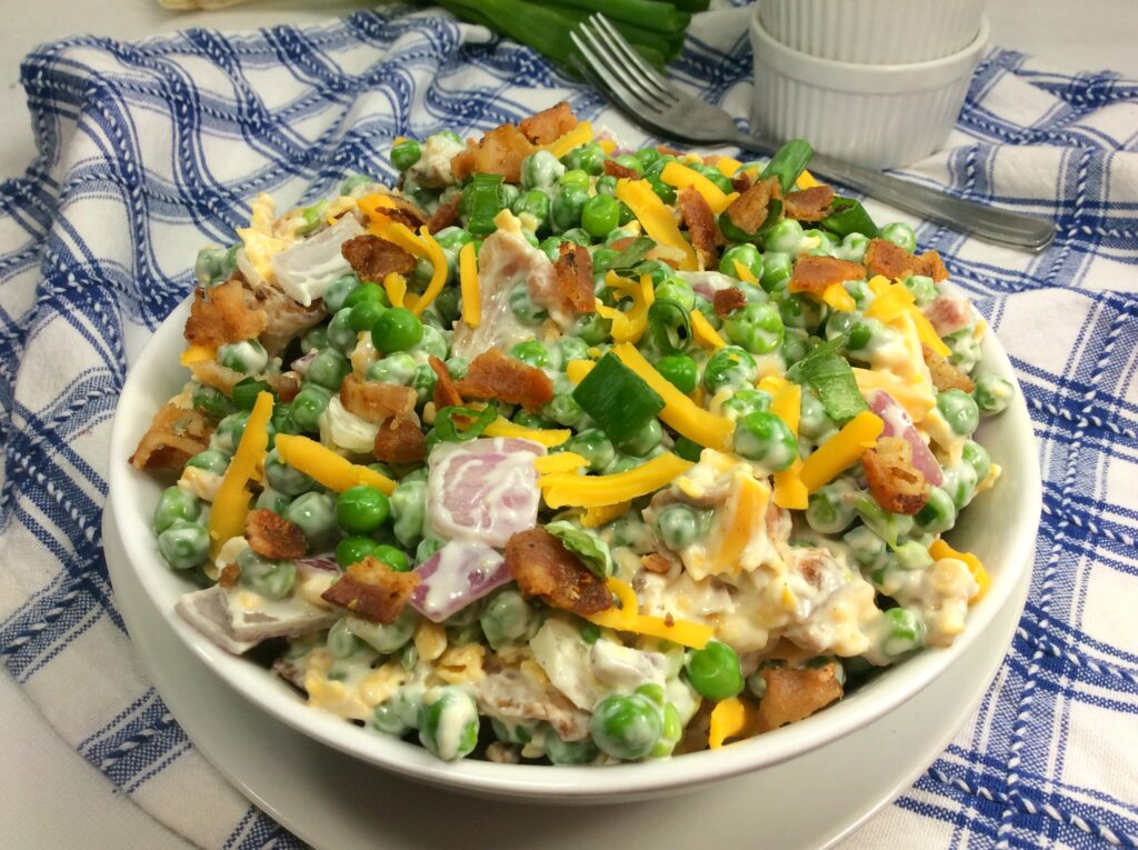 A colorful bowl of Simple Pea, Bacon and Cheddar Salad set on a blue and white tablecloth.