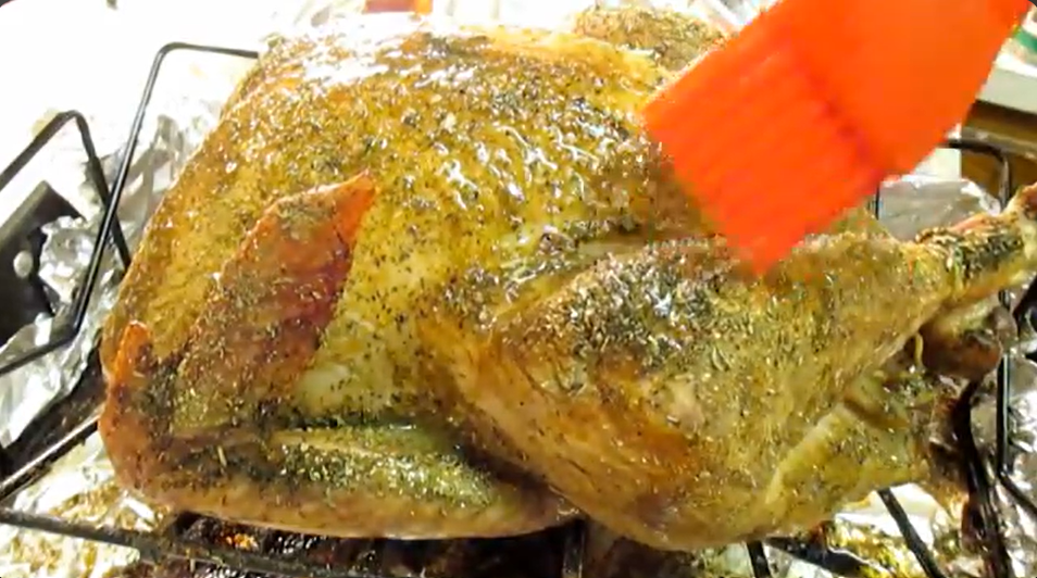 Rosie uses a red silicon basting brush to baste the partially roasted Thanksgiving turkey with more flavorful herb butter.