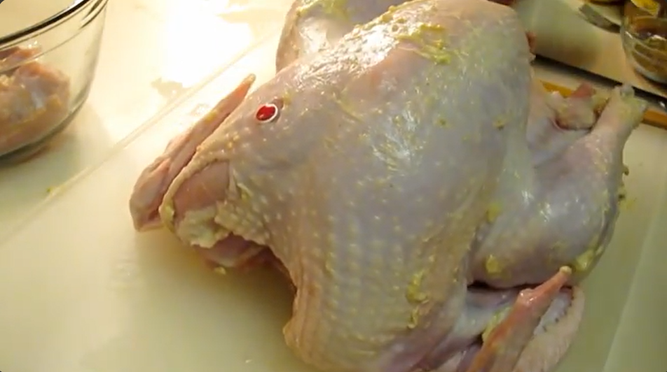 A raw whole turkey sits on a cutting board, the skin covered in a savory herb butter mixture.