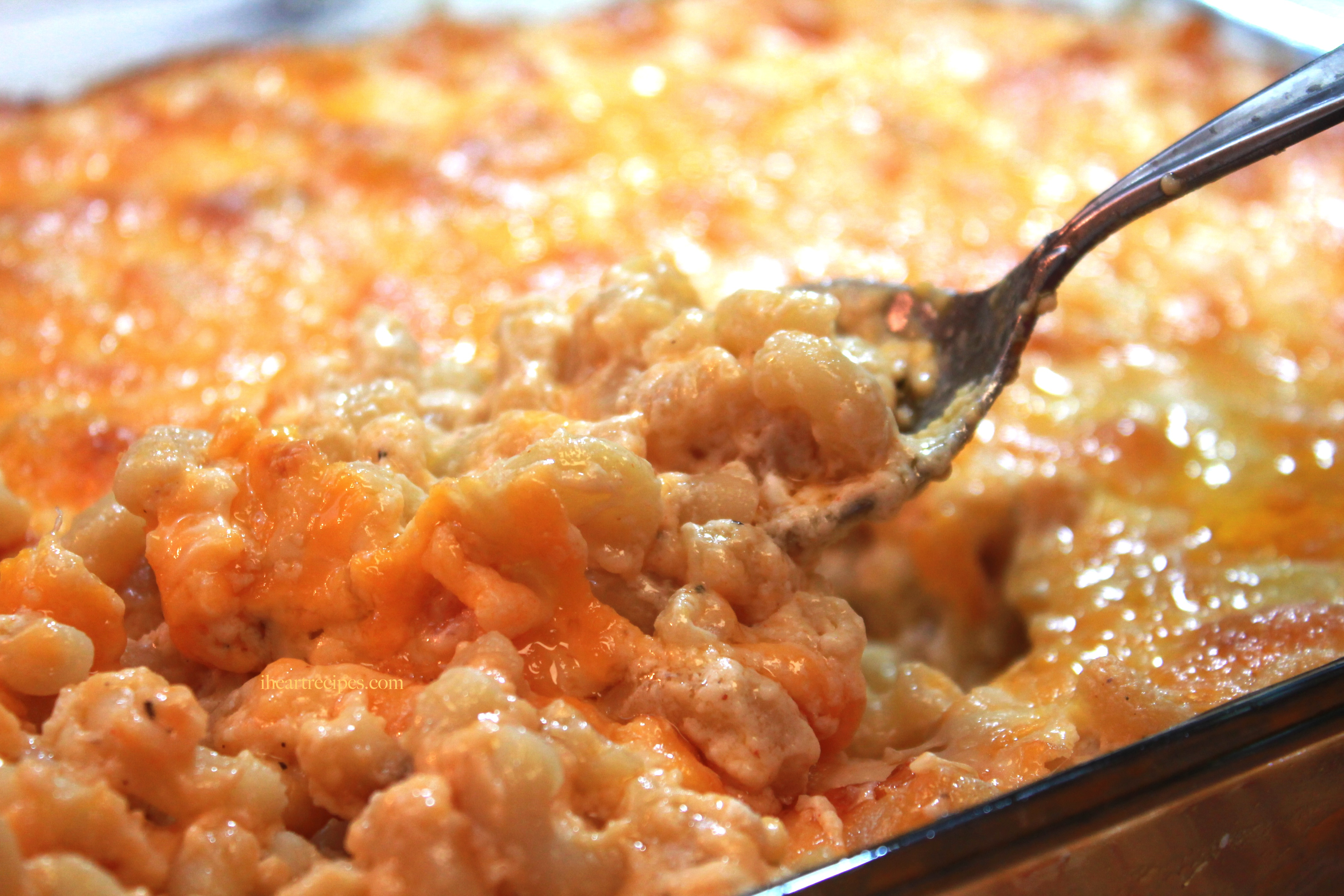 A serving spoon scoops a spoonful of Southern style baked macaroni and cheese from a glass casserole dish.