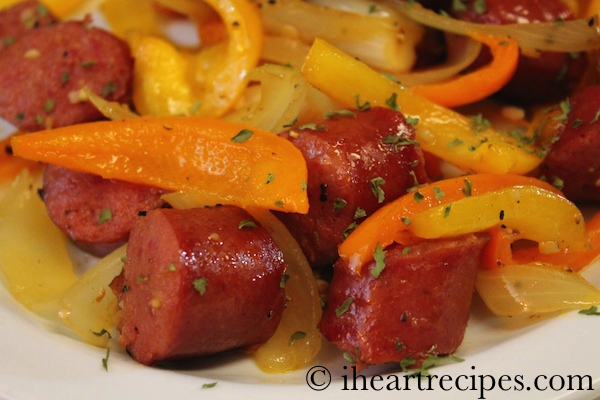 A close up image of pan-fried sausage and peppers seasoned with Italian seasoning, served on a white plate.