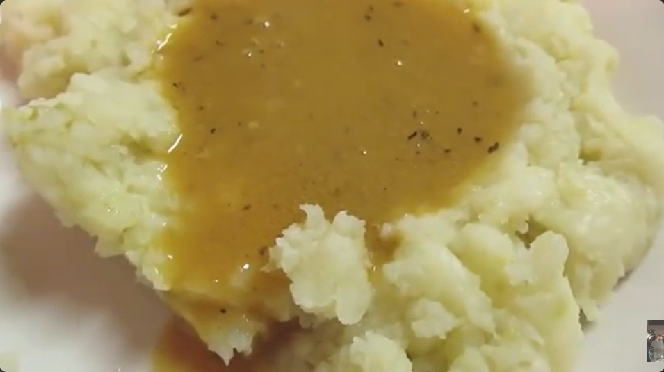 A closeup image of mashed potatoes topped with a homemade turkey gravy, made with tasty pan drippings.